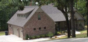 A brick home with a garage in the middle of a wooded area.