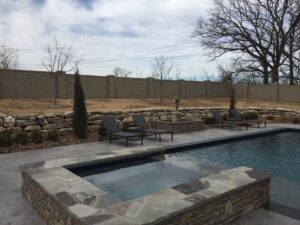 A backyard with a pool and a stone wall.