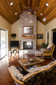 A living room with a stone fireplace and ceiling fan.